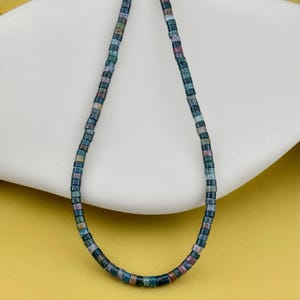 May include: A necklace composed of small, cylindrical beads in a variety of muted earth tones, including shades of deep blue, forest green, dusty rose, and charcoal gray. The beads are strung together in a continuous, uniform strand.