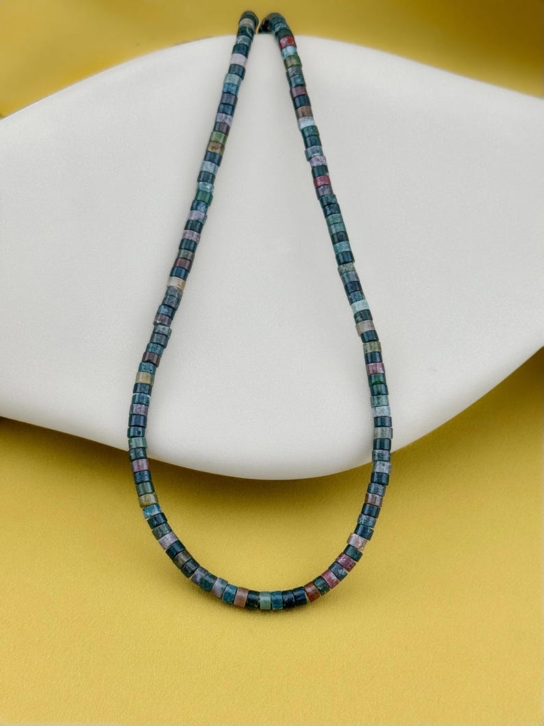 May include: A necklace composed of small, cylindrical beads in a variety of muted earth tones, including shades of deep blue, forest green, dusty rose, and charcoal gray. The beads are strung together in a continuous, uniform strand.