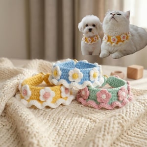 May include: Three crocheted pet collars featuring a ruffled edge and floral appliques. One collar is yellow with white and pink flowers, one is light blue with white and yellow flowers, and one is mint green with pink and white flowers.
