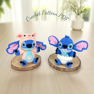 Könnte beinhalten: Zwei gehäkelte Figuren einer blauen, außerirdischen Figur, eine mit einem rosa Schweinehut. Sie haben große Ohren und sitzen auf Holzscheiben. Der Text "Crochet Pattern PDF" steht darüber.