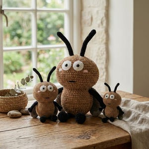 May include: Three brown crochet insect dolls with large white eyes, black pupils, and two black antennae each. The dolls feature round bodies, small black feet, and grey wings. The central doll is the largest, flanked by two smaller identical dolls.