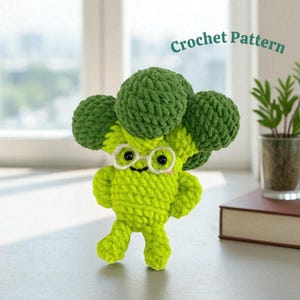 May include: A handmade crochet broccoli figure in shades of green and yellow. The broccoli has a smiling face, small glasses, and arms and legs. The text "Crochet Pattern" is above the broccoli.