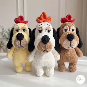 Peut inclure: Trois jouets en peluche pour chiens faits à la main au crochet, debout côte à côte. Chaque chien présente de longues oreilles noires, un nez noir et une petite touffe de laine rouge ou orange sur la tête. Les chiens sont en laine jaune clair, blanche et marron clair.