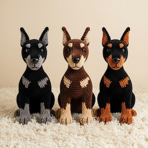 Könnte beinhalten: Drei handgefertigte Dobermann Pinscher Hundefiguren aus Häkelarbeit. Die Hunde sind in Schwarz, Braun und Schwarz mit braunen Markierungen gehalten. Jeder Hund hat aufrechte Ohren und sitzt auf einer weißen, strukturierten Oberfläche. Die Hunde sind ein einzigartiger Einrichtungsgegenstand.