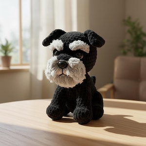 Pu&ograve; includere: Un giocattolo per cani all'uncinetto nero e grigio fatto a mano, simile a uno Schnauzer. Il peluche ha un corpo, una testa e orecchie neri, con accenti grigi sul muso e sulle sopracciglia. &Egrave; posizionato su una superficie di legno.