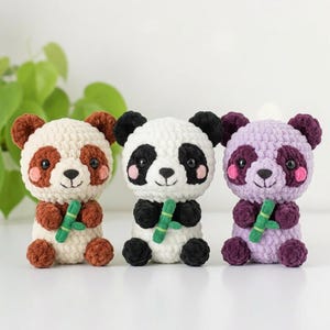 May include: Three crocheted plush panda toys made of soft yarn. The left panda is cream and brown, the centre panda is white and black, and the right panda is light purple and dark purple. Each panda holds a small green crocheted bamboo stalk.