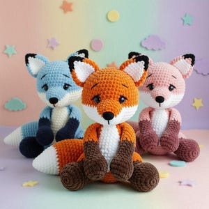 Puede incluir: Tres zorros de crochet hechos a mano en azul, naranja y rosa. Cada zorro tiene una cara blanca, ojos negros y una cola esponjosa. El zorro naranja está en el centro, con los zorros azul y rosa a cada lado. El fondo es pastel con formas de estrellas y nubes.