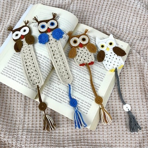 May include: Four handmade crochet owl bookmarks in various colours, including brown, white, and blue. Each bookmark features an owl design with a tassel. The bookmarks are placed on the pages of an open book.