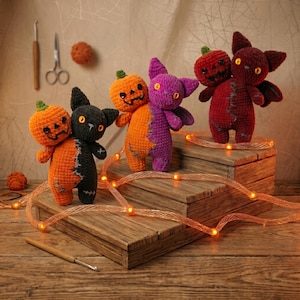May include: Three handmade crochet plush toys featuring two-headed designs. One is orange and black, one is orange and purple, and one is dark red. Each creature has button eyes and stitched details. They are displayed on a wooden tiered stand.