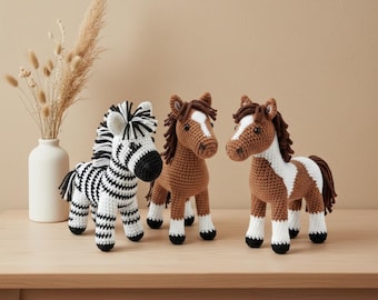 May include: Three crocheted animal figures: a zebra with black and white stripes, and two brown horses with white markings. The figures are displayed on a light-colored wooden surface.