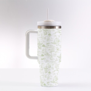 Peut inclure: Un mug de voyage blanc avec une poignée et un couvercle, orné d'un motif de toile de Jouy vert. Le mug comprend une paille blanche et un bord argenté. Le motif représente une scène pastorale avec des personnages, des arbres et des bâtiments.