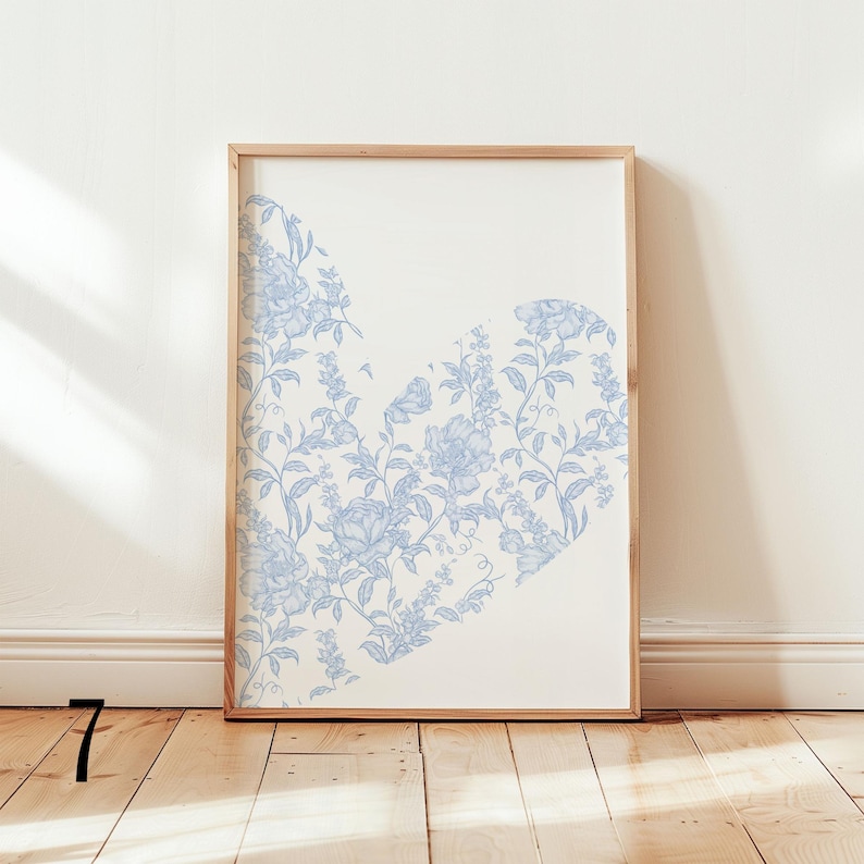 May include: Framed art print featuring a heart-shaped design filled with light blue floral patterns on a cream background. The artwork is encased in a natural wood frame, adding a touch of elegance to the piece. The print is displayed against a white wall.