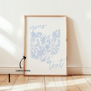May include: A framed print featuring a floral design in the shape of the state of Ohio. The print is in a light blue color, with the words "your" and "text" in a script font. The words "Custom State" are also visible.