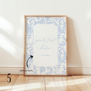 May include: A framed print with a light wood frame. The print features a floral design in light blue and white. The center has the words "your text here" and "est. 1809". The words "custom text" are written on the bottom left.