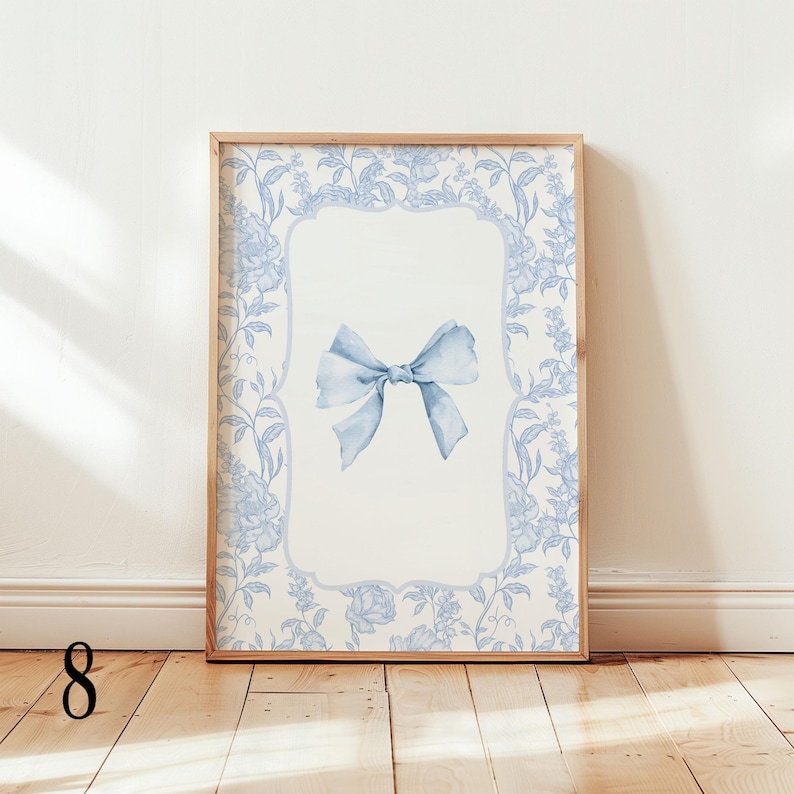 May include: A framed art print featuring a light blue watercolor bow on a white background. The frame is surrounded by a floral pattern in light blue. The artwork is displayed in a wooden frame, adding a touch of elegance to the piece.