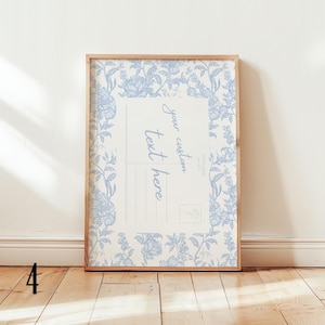 May include: A framed print featuring a vintage postcard design. The print has a light beige background with a blue floral border and the words "your custom text here". The frame is made of light-colored wood.
