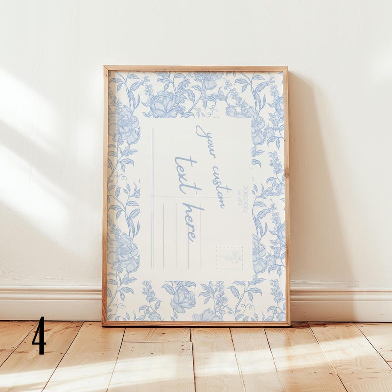 May include: A framed print featuring a vintage postcard design. The print has a light beige background with a blue floral border and the words "your custom text here". The frame is made of light-colored wood.