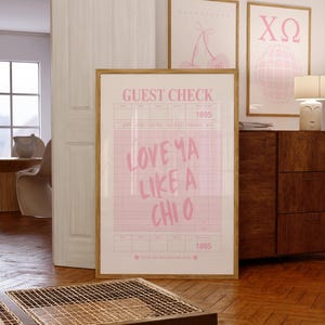 Può includere: Una stampa rosa incorniciata con le parole "LOVE YA LIKE A CHI O" in stile scritto a mano, simile a un conto del ristorante. La stampa è in una cornice di legno ed è esposta con altre stampe incorniciate con disegni rosa.