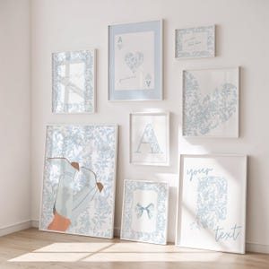 May include: A collection of framed art prints in various sizes, featuring a consistent light blue and white floral pattern. Some prints display playing card suits, an initial, a bow, and text. The artwork is displayed on a white wall.