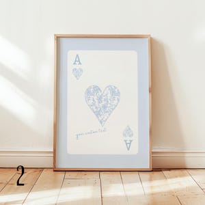 May include: Framed Ace of Hearts art print. The playing card features a light blue floral heart design and matching suit symbols. The text "your custom text" is printed at the bottom of the card. The print is framed in a light wood frame.
