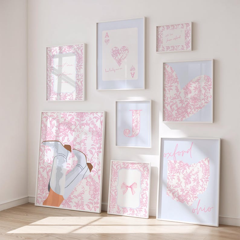May include: A collection of framed art prints in various sizes, featuring a consistent pink and white color scheme. The prints include floral patterns, playing card designs, a bow, a heart-shaped Ohio outline, and the letter "J".