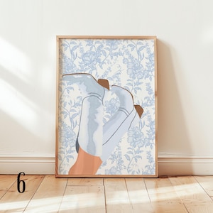 May include: A framed art print featuring an illustration of light blue cowboy boots with brown accents, set against a blue floral wallpaper background. The artwork is displayed in a wooden frame, adding a touch of rustic charm.