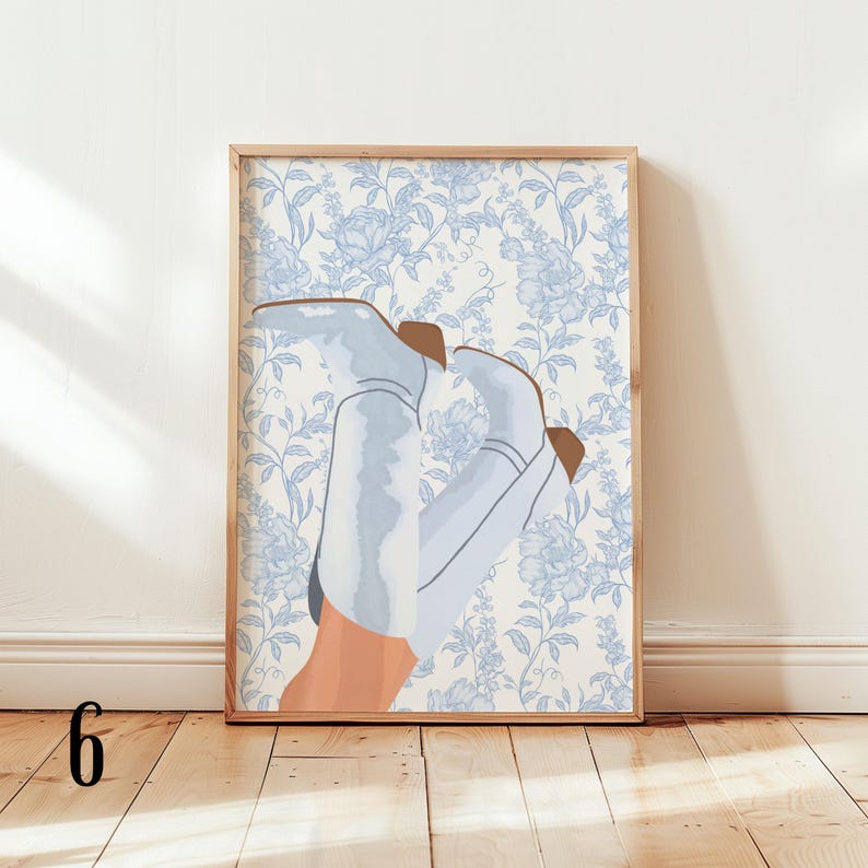 May include: A framed art print featuring an illustration of light blue cowboy boots with brown accents, set against a blue floral wallpaper background. The artwork is displayed in a wooden frame, adding a touch of rustic charm.