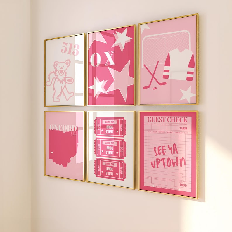 Op de afbeelding: Een set van acht roze en witte ingelijste prints met verschillende ontwerpen, waaronder een beer, sterren, een hockeynet, een ticketstub, een kaart van Ohio en een gastcheque. De prints hebben gouden lijsten en zijn in een rasterpatroon op een witte muur gerangschikt.