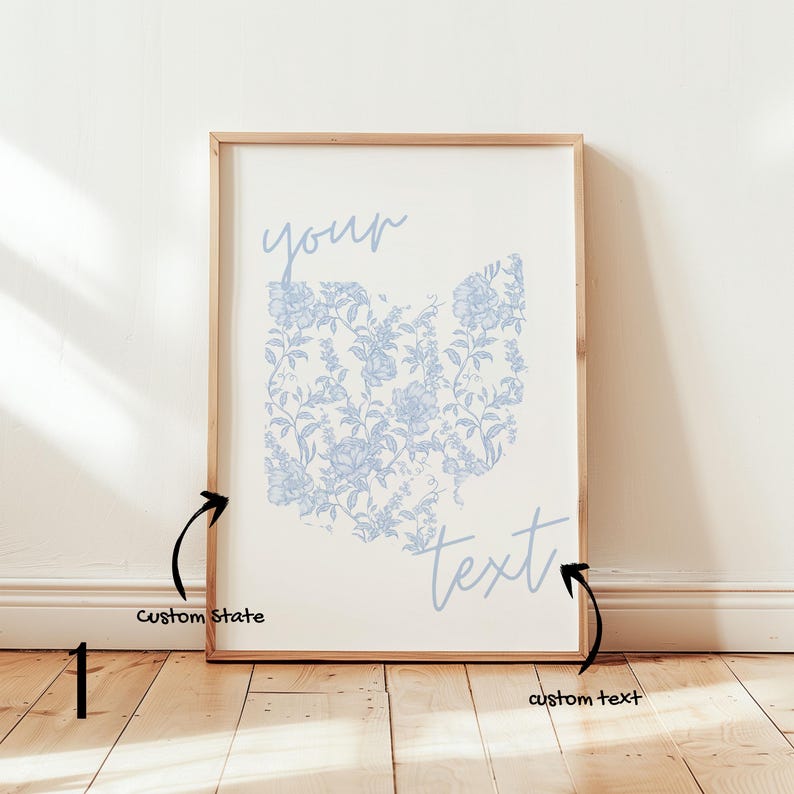 May include: A framed print featuring a floral design in the shape of Ohio, in light blue on a cream background. The words "your" and "text" are written in a script font. The frame is made of light wood.
