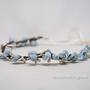 May include: A light blue flower crown with white accents. The crown is made of fabric flowers and is tied with a white ribbon.