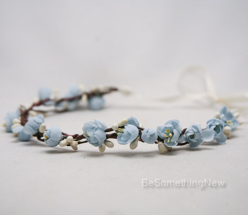 May include: A light blue flower crown with white accents. The crown is made of fabric flowers and is tied with a white ribbon.
