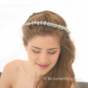 Pu&ograve; includere: Un cerchietto floreale argentato con piccole rose di tessuto delicate. Il cerchietto &egrave; indossato da una donna con i capelli lunghi e castani.