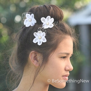 May include: White lace flower hair clips with pearl centers. The clips are worn in a woman's hair.