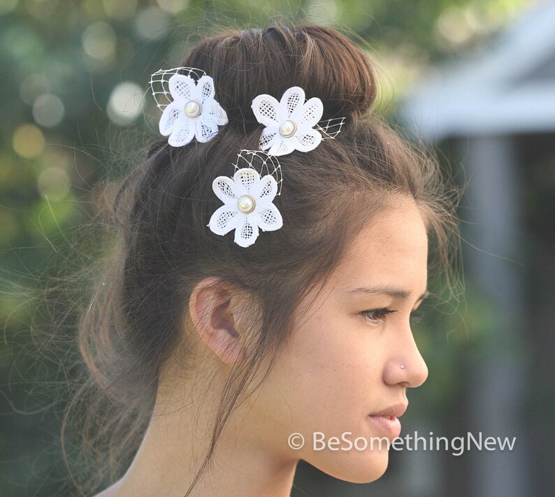 May include: White lace flower hair clips with pearl centers. The clips are worn in a woman's hair.