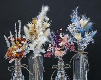Op de afbeelding: Vier glazen flessen met gedroogde bloemenarrangementen. De flessen zijn van helder glas met een getextureerd oppervlak. De bloemen zijn in verschillende kleuren, waaronder wit, roze, blauw en oranje.