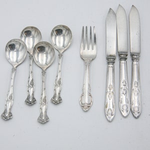 Puede incluir: Un juego de cubiertos de plata que incluye cuatro cucharaditas y tres cuchillos, junto con un tenedor. Los cubiertos tienen un diseño adornado con un patrón floral.