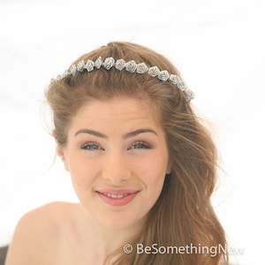 Pu&ograve; includere: Un cerchietto floreale argentato con piccole rose bianche in tessuto. Il cerchietto &egrave; indossato da una donna con i capelli lunghi e castani.