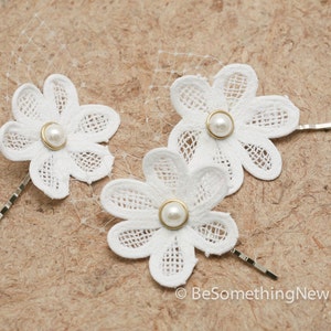 May include: Three white lace flower hair clips with pearl centers. Each clip has a gold-toned pin.