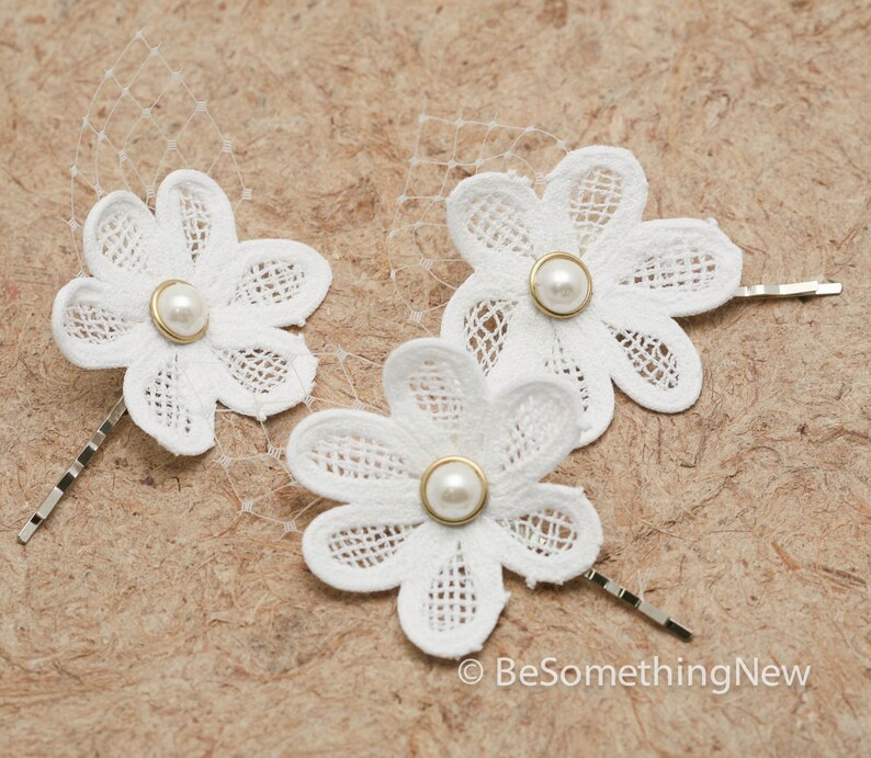 May include: Three white lace flower hair clips with pearl centers. Each clip has a gold-toned pin.