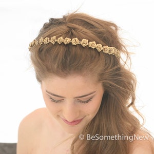 May include: A gold headband with small, delicate fabric rose embellishments. The headband is worn by a person with long, wavy, light brown hair.