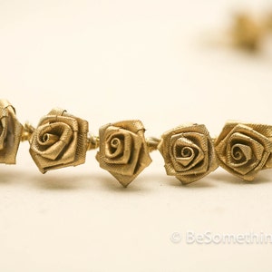 May include: A gold-coloured garland of fabric roses, strung together with wire. The roses are small and have a delicate, vintage look.