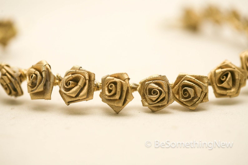 May include: A gold-coloured garland of fabric roses, strung together with wire. The roses are small and have a delicate, vintage look.