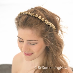 May include: A gold headband with small rose-shaped embellishments. The headband is worn by a person with long, brown hair.