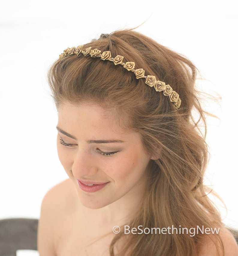 May include: A gold headband with small rose-shaped embellishments. The headband is worn by a person with long, brown hair.