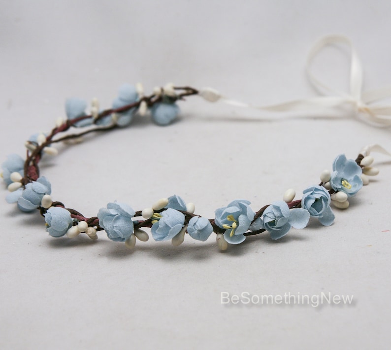 May include: A light blue floral crown with white accents. The crown is made of fabric flowers and is tied with a white ribbon.