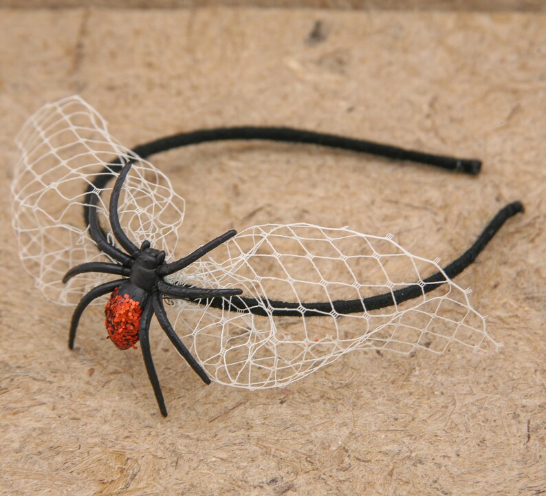 May include: A black headband with a decorative black spider and white netting. The spider has a red glitter abdomen. This Halloween-themed accessory is perfect for costumes and themed events.