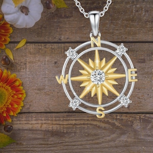 May include: A silver and gold compass pendant necklace with a starburst design and clear crystals. The compass points north, south, east, and west.