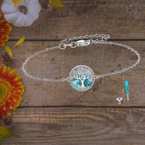 Può includere: Bracciale color argento con un ciondolo rotondo raffigurante un albero della vita. Il ciondolo ha uno sfondo di conchiglia di abalone blu e verde con dettagli floreali arancioni e rossi. Include piccoli strumenti e accessori.