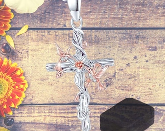 May include: Silver and rose gold toned pendant necklace featuring a cross with a vine design and two hummingbirds with clear crystal accents.