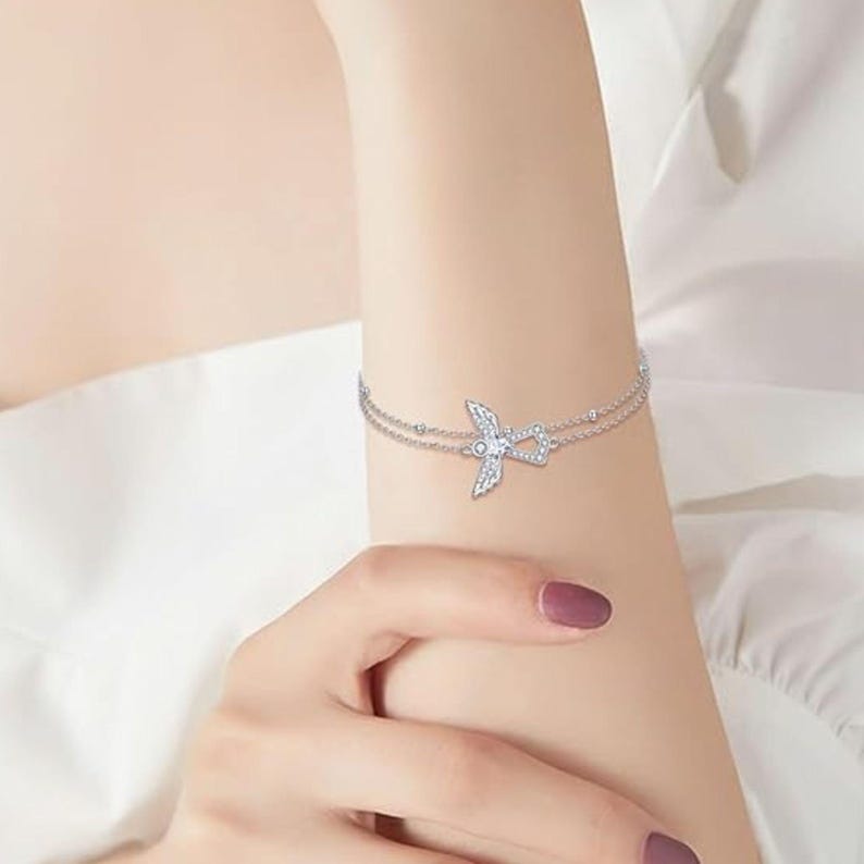May include: A silver bracelet featuring a dainty angel wing charm set with sparkling cubic zirconia stones.